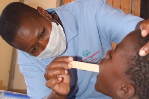 A close-up picture of a doctor and young boy. The doctor uses a tongue depressor to look into the boy's mouth. The doctor is wearing a Special Olympics shirt.