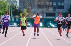 5 runners race toward the finish line and straight toward the camera  on an outdoor track. 